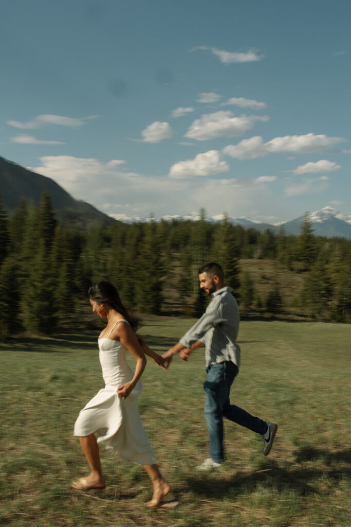 Candid engagement photo of couple exploring Glacier National Park with snowy peaks and spring landscape