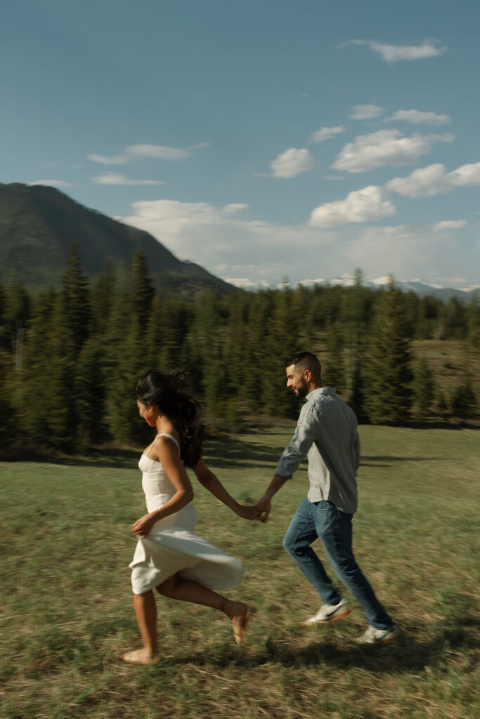 Candid engagement photo of couple exploring Glacier National Park with snowy peaks and spring landscape
