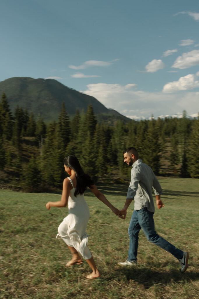 Candid engagement photo of couple exploring Glacier National Park with snowy peaks and spring landscape
