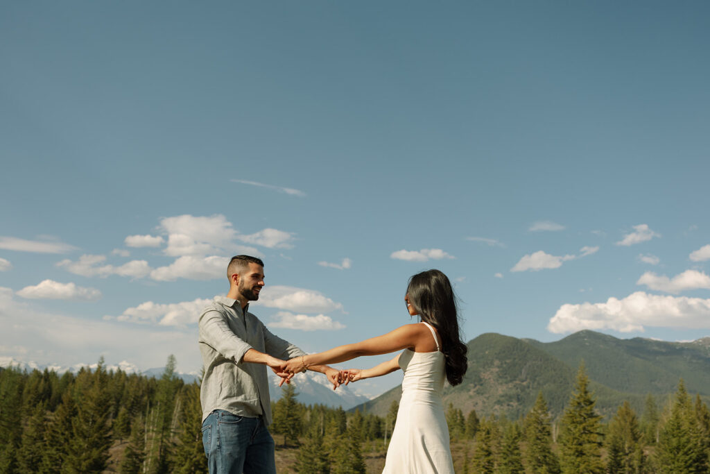 Candid engagement photo of couple exploring Glacier National Park with snowy peaks and spring landscape
