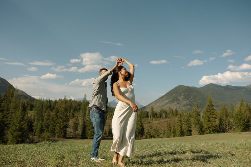 Couple walking through lush green valley with snow-capped mountains during a Glacier National Park engagement session
