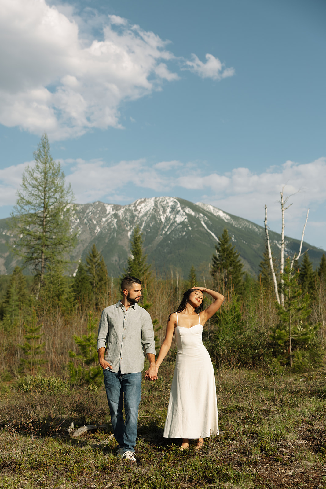 Couple walking through lush green valley with snow-capped mountains during a Glacier National Park engagement session