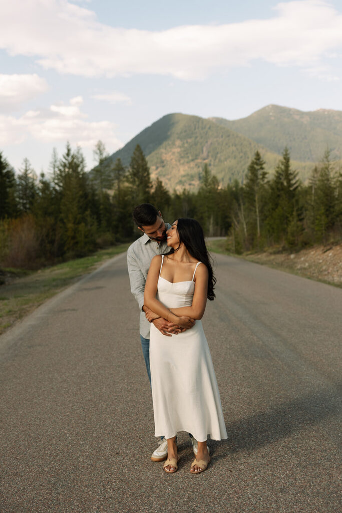Couple walking through lush green valley with snow-capped mountains during a Glacier National Park engagement session