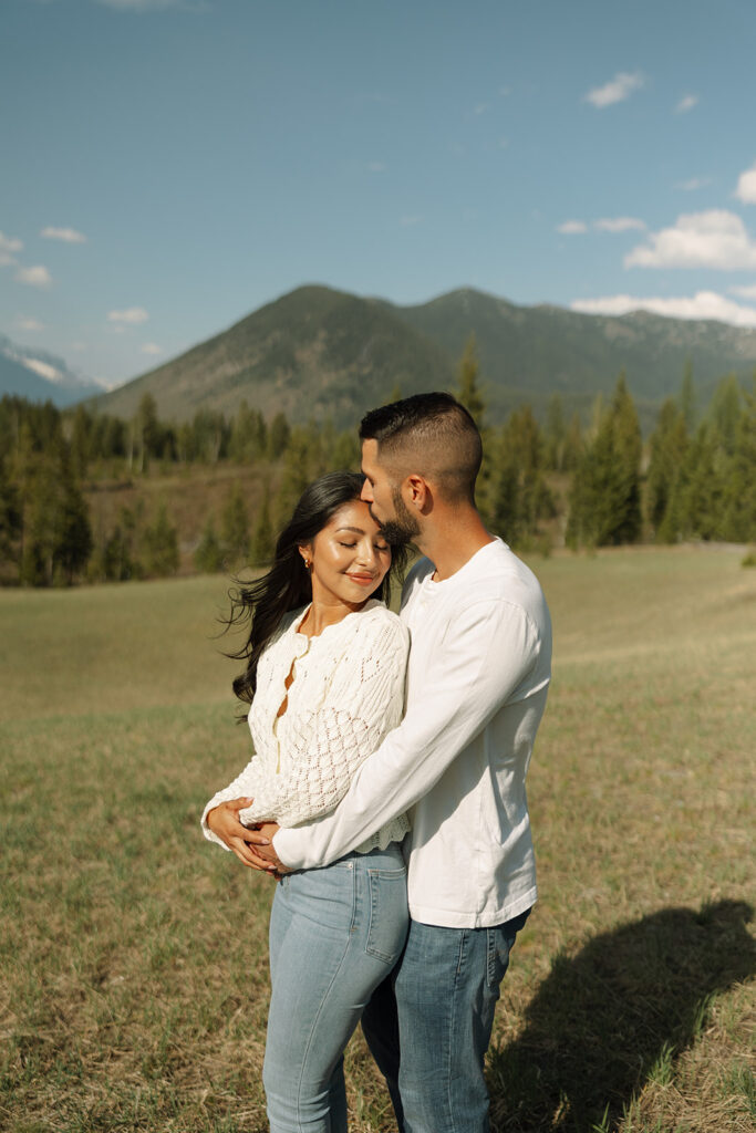 Couple walking through lush green valley with snow-capped mountains during a Glacier National Park engagement session
