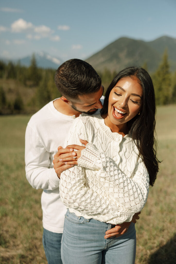 Couple walking through lush green valley with snow-capped mountains during a Glacier National Park engagement session