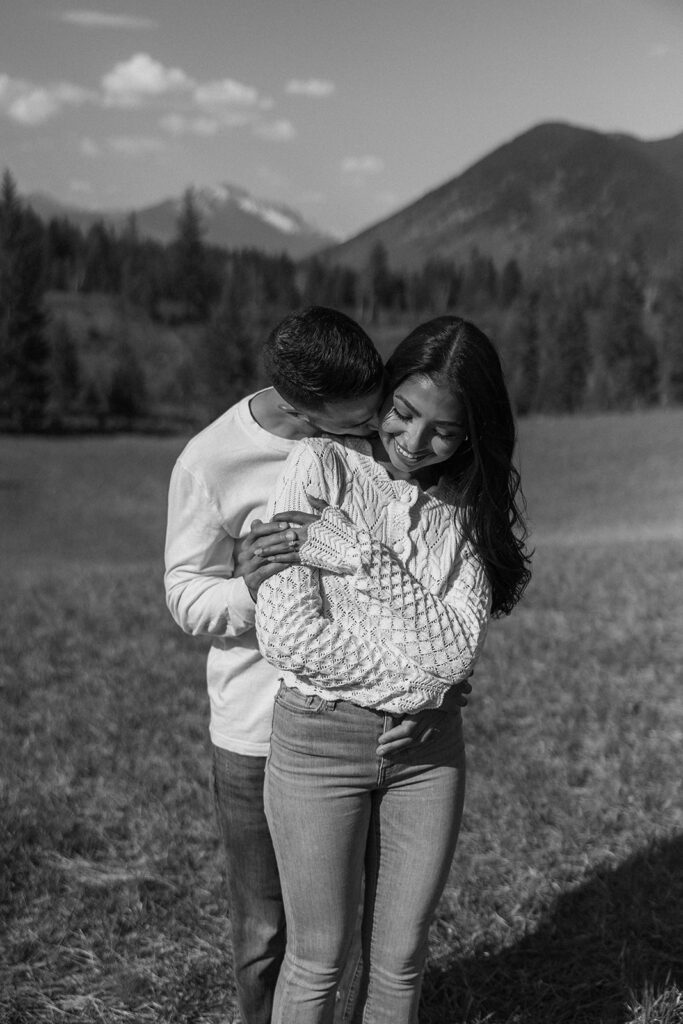 Couple walking through lush green valley with snow-capped mountains during a Glacier National Park engagement session