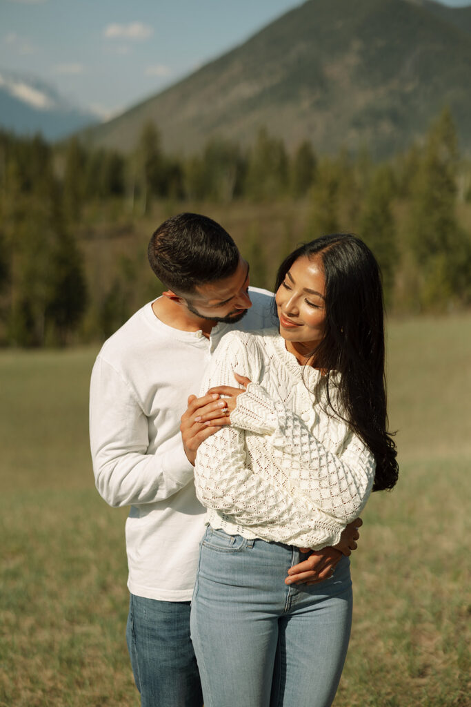 Couple walking through lush green valley with snow-capped mountains during a Glacier National Park engagement session