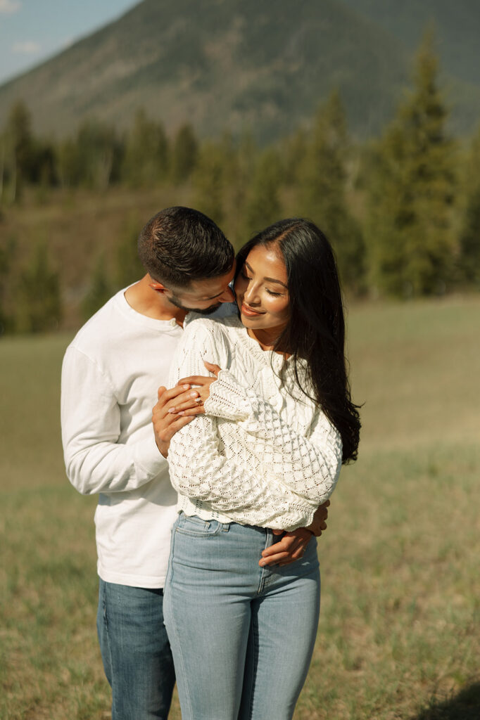Couple walking through lush green valley with snow-capped mountains during a Glacier National Park engagement session