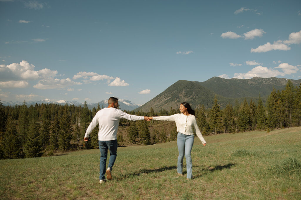 Couple holding hands in a wide open landscape during their Glacier National Park engagement session

