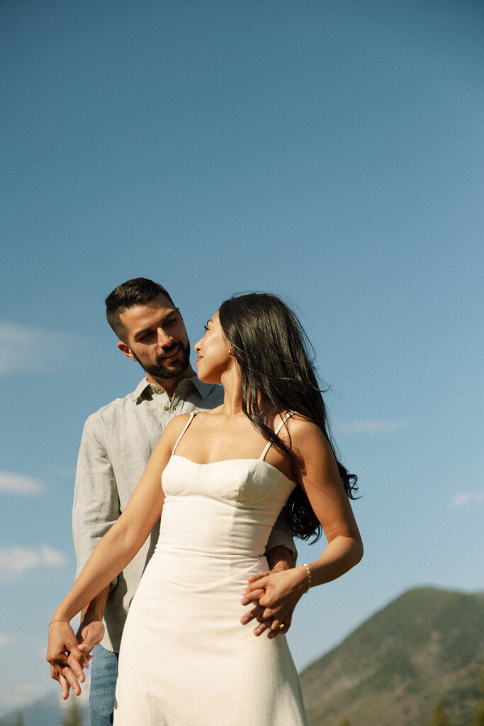 Candid engagement photo of couple exploring Glacier National Park with snowy peaks and spring landscape
