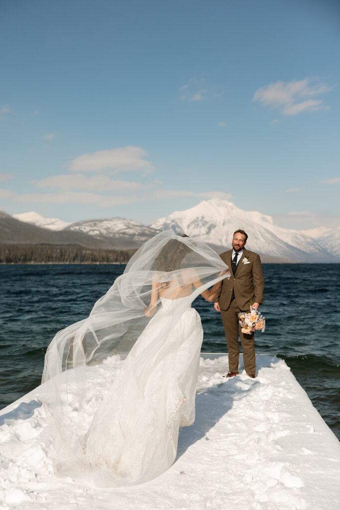 A winter elopement at Lake McDonald with a couple standing by a snowy lakeshore surrounded by mountains
