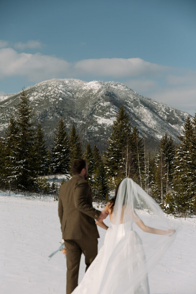 A winter elopement at Lake McDonald with a couple standing by a snowy lakeshore surrounded by mountains