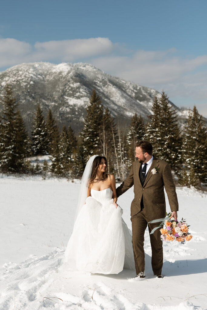 Couple walking along a frozen lake in Glacier National Park during a romantic winter elopement
