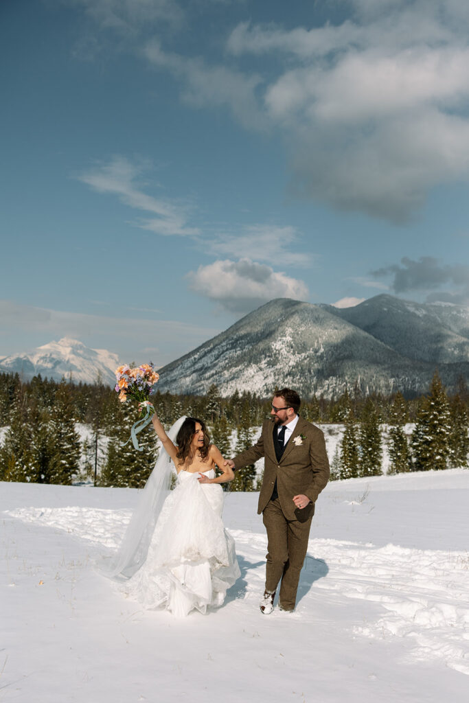 A winter elopement at Lake McDonald with a couple standing by a snowy lakeshore surrounded by mountains