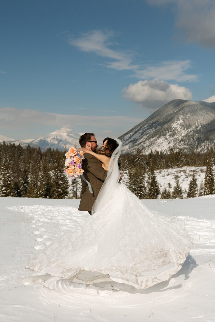 A winter elopement at Lake McDonald with a couple standing by a snowy lakeshore surrounded by mountains
