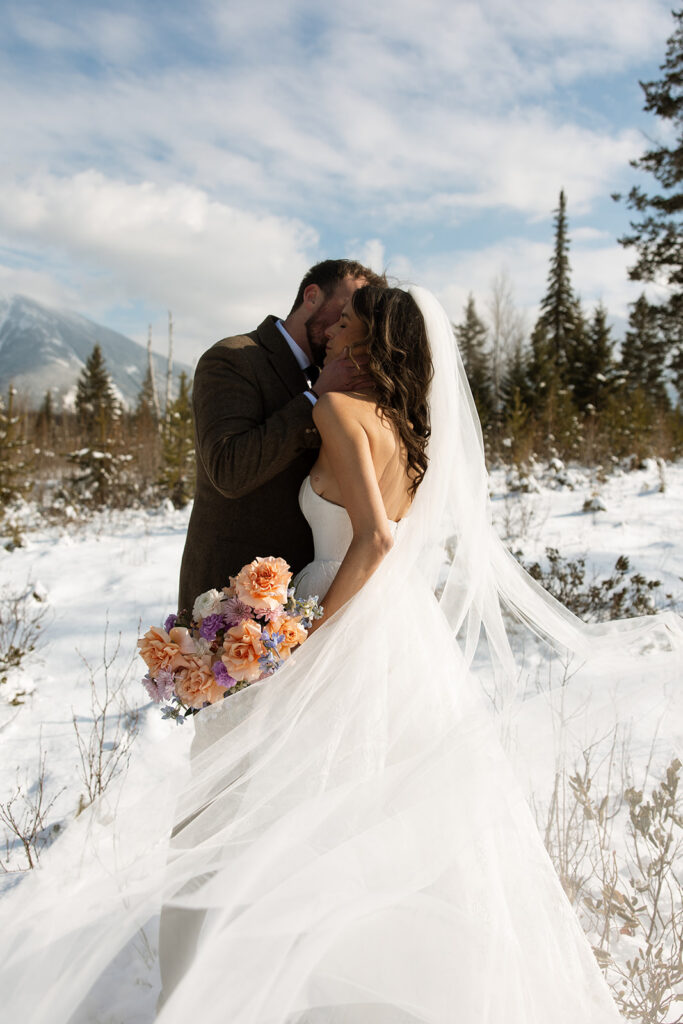 A winter elopement at Lake McDonald with a couple standing by a snowy lakeshore surrounded by mountains

