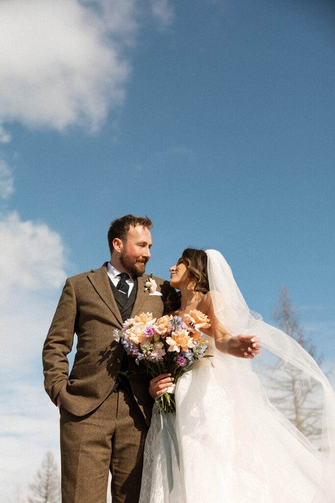 A winter elopement at Lake McDonald with a couple standing by a snowy lakeshore surrounded by mountains
